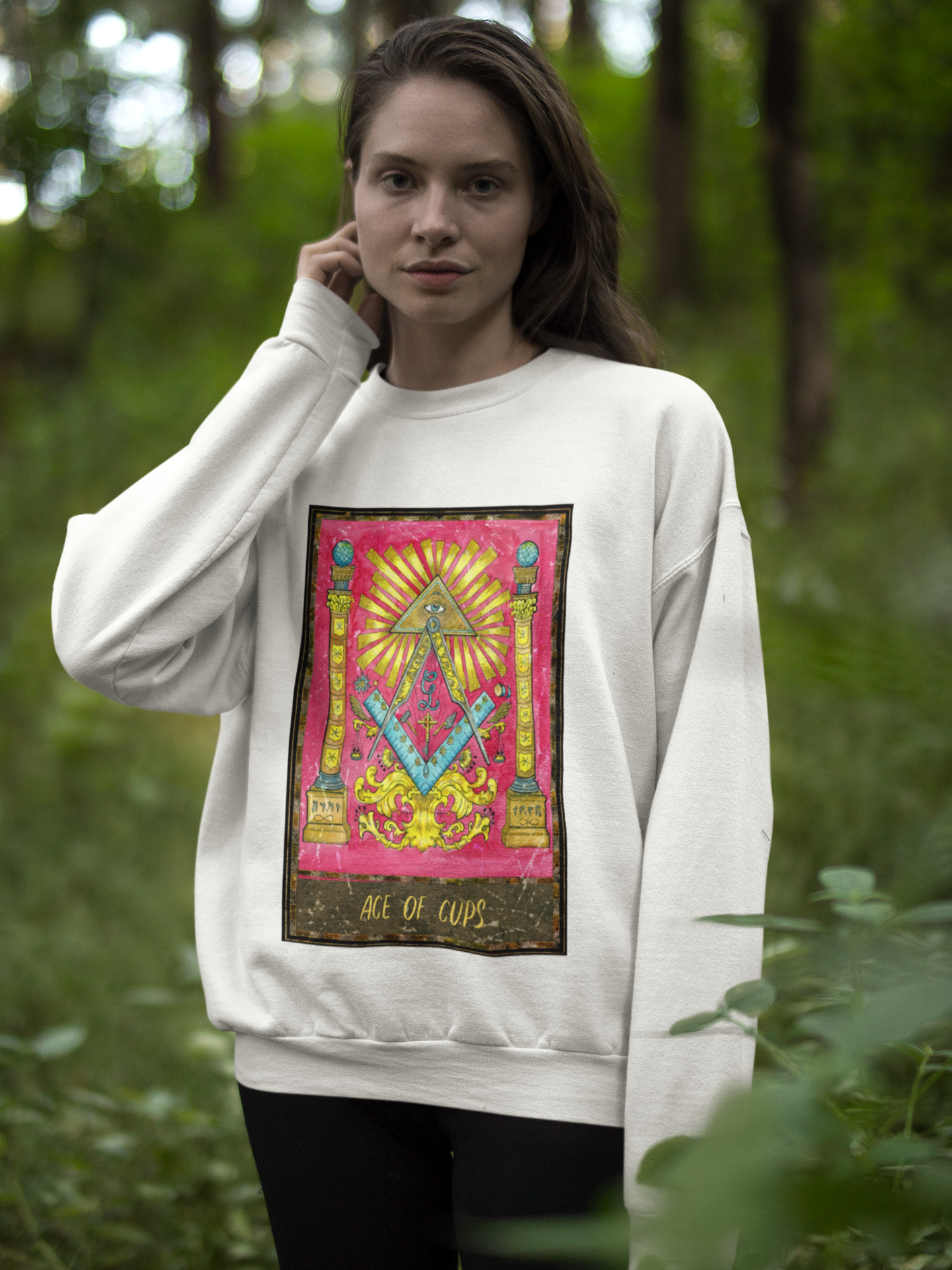 white woman wearing a white crew neck Ace of Cups Tarot Card Sweatshirt, black pants standing in the woods